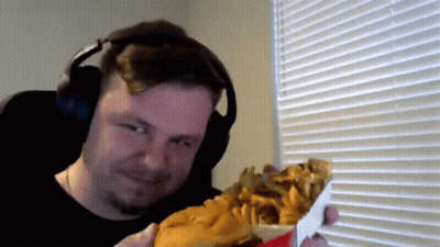 A Man Wearing Headphones Is Holding A Large Hamburger And French Fries GIF