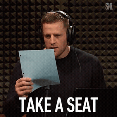 A Man Wearing Headphones Is Holding A Piece Of Paper With The Words Take A Seat Written On It . GIF