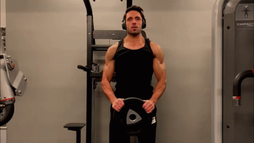 A Man Wearing Headphones Is Holding A Weight Plate With An Arrow On It GIF