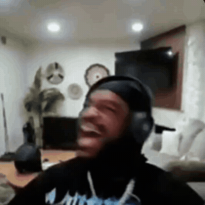 A Man Wearing Headphones Is Laughing In A Living Room While Sitting On A Couch . GIF