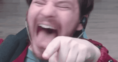A Man Wearing Headphones Is Laughing With His Mouth Open And Pointing At The Camera . GIF