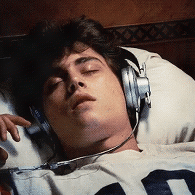 A Man Wearing Headphones Is Laying In Bed GIF