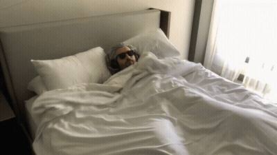 A Man Wearing Headphones Is Laying On A Bed GIF