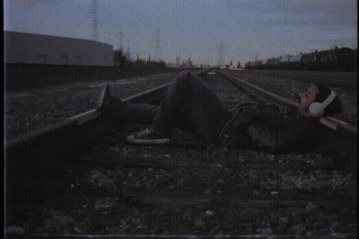 A Man Wearing Headphones Is Laying On The Train Tracks GIF
