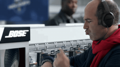 A Man Wearing Headphones Is Looking At His Watch In Front Of A Bose Sign GIF