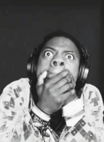 A Man Wearing Headphones Is Making A Funny Face While Covering His Mouth . GIF