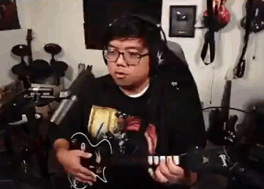 A Man Wearing Headphones Is Playing A Guitar In Front Of A Microphone In A Room . GIF