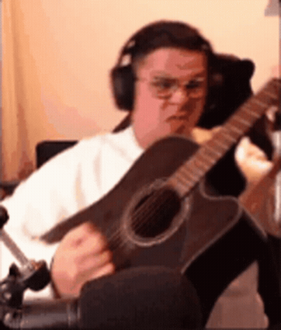 A Man Wearing Headphones Is Playing An Acoustic Guitar In A Room . GIF