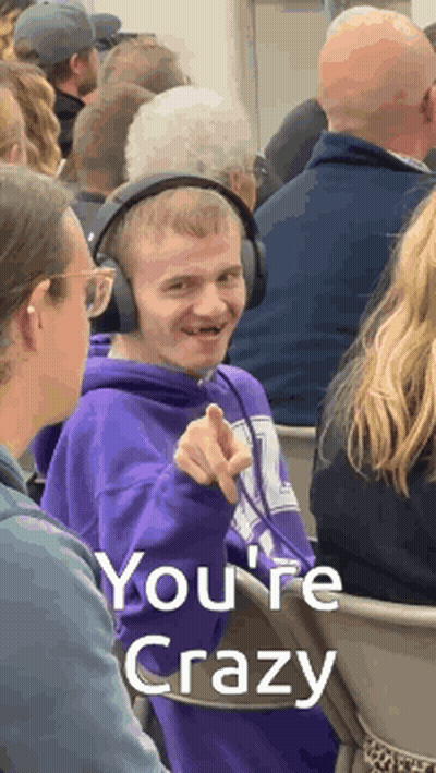 A Man Wearing Headphones Is Pointing At The Camera With The Words You 'Re Crazy Behind Him GIF