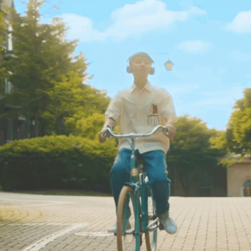 A Man Wearing Headphones Is Riding A Bicycle On A Brick Road GIF