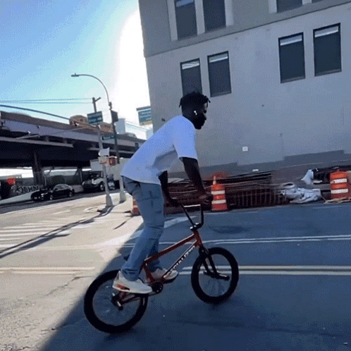 A Man Wearing Headphones Is Riding A Bicycle On A Street GIF