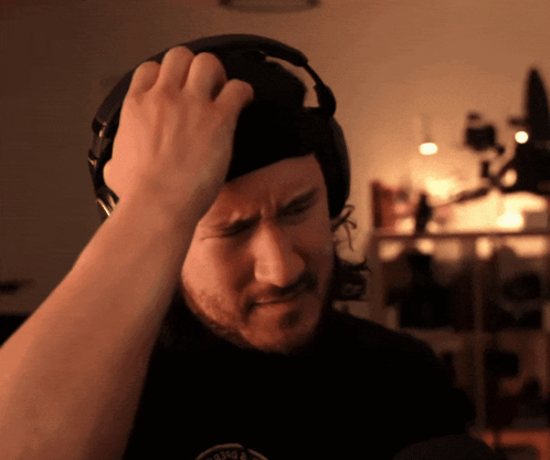 A Man Wearing Headphones Is Scratching His Head GIF
