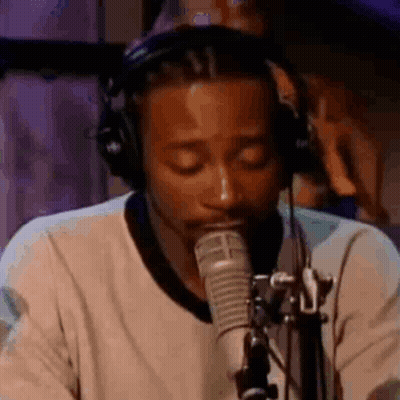A Man Wearing Headphones Is Singing Into A Microphone In A Studio . GIF