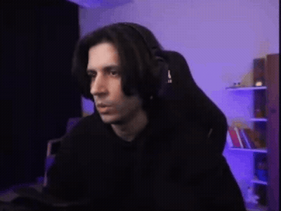 A Man Wearing Headphones Is Sitting In A Gaming Chair In Front Of A Computer . GIF