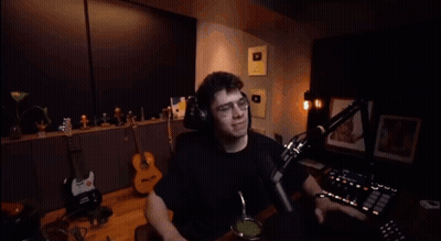 A Man Wearing Headphones Is Sitting In Front Of A Microphone And Waving His Hand GIF