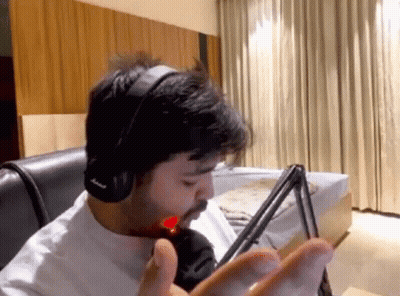 A Man Wearing Headphones Is Sitting In Front Of A Microphone In A Living Room . GIF