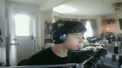 A Man Wearing Headphones Is Sitting In Front Of A Microphone In A Room GIF