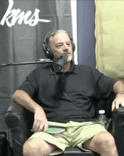 A Man Wearing Headphones Is Sitting In Front Of A Microphone In Front Of A Sign That Says Kns GIF