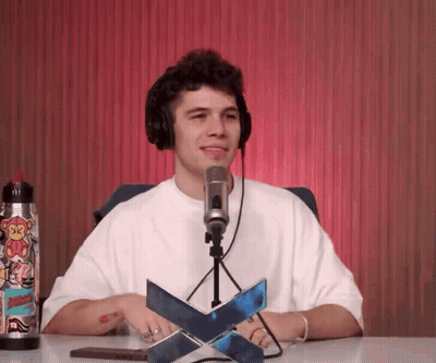 A Man Wearing Headphones Is Sitting In Front Of A Microphone With A Sticker On His Water Bottle That Says Sk GIF