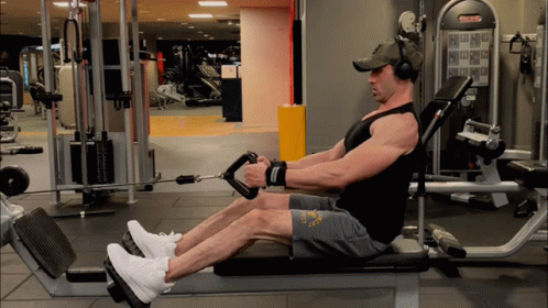 A Man Wearing Headphones Is Sitting On A Bench In A Gym With A Machine That Says ' Matrix ' On It GIF