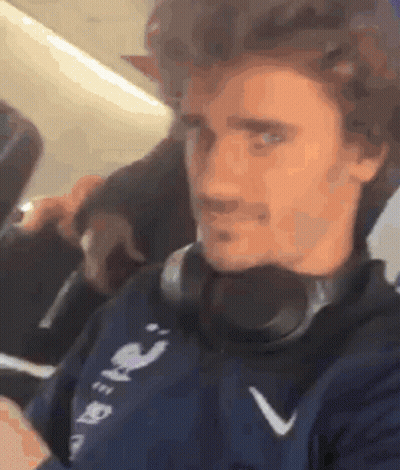 A Man Wearing Headphones Is Sitting On A Plane And Looking At His Phone . GIF