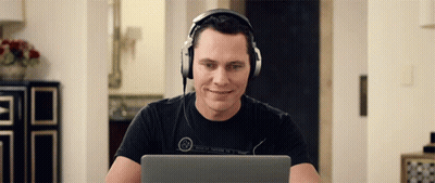 A Man Wearing Headphones Is Smiling While Looking At His Laptop GIF