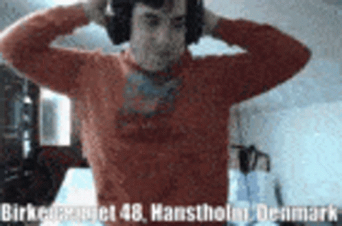 A Man Wearing Headphones Is Standing In A Room With His Hands On His Head GIF