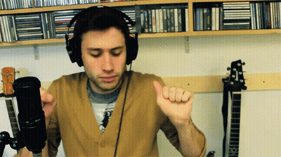 A Man Wearing Headphones Is Standing In Front Of A Microphone And Giving A Thumbs Up GIF