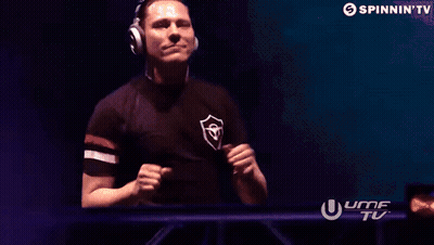 A Man Wearing Headphones Is Standing In Front Of A Screen That Says Spinnin ' Tv . GIF