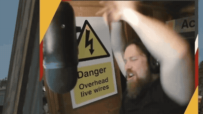 A Man Wearing Headphones Is Standing In Front Of A Sign That Says Danger Overhead Live Wires GIF