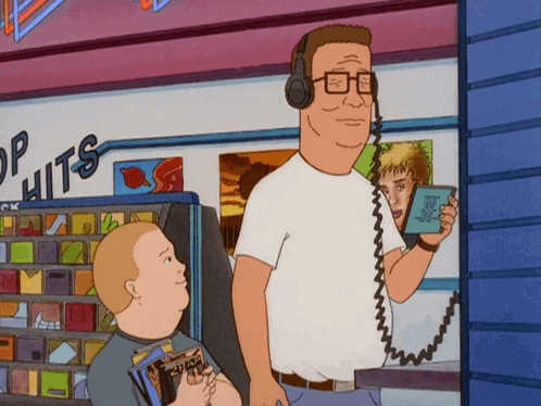 A Man Wearing Headphones Is Standing In Front Of A Store That Says " Top Hits " GIF