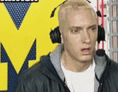 A Man Wearing Headphones Is Standing In Front Of A Yellow M GIF