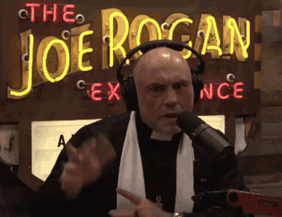 A Man Wearing Headphones Is Talking Into A Microphone In Front Of A Neon Sign That Says The Joe Rogan GIF
