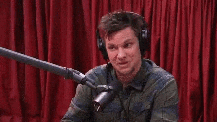 A Man Wearing Headphones Is Talking Into A Microphone In Front Of A Red Curtain GIF
