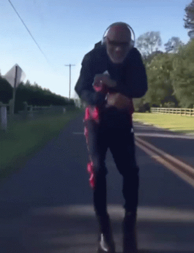 A Man Wearing Headphones Is Walking Down A Street GIF