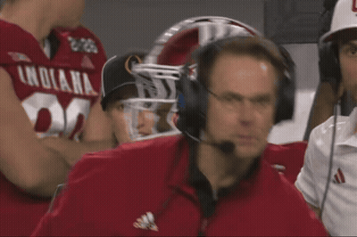 A Man Wearing Headphones Is Watching A Football Game With A Player Wearing A Jersey That Says Nebraska GIF