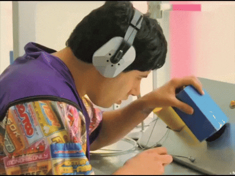 A Man Wearing Headphones Looks At A Blue Box That Says Monopoly On It GIF