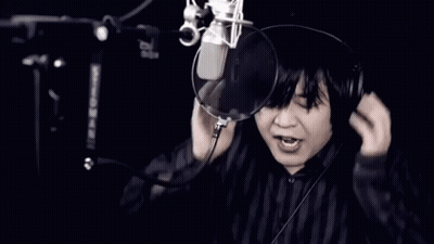 A Man Wearing Headphones Singing Into A Microphone With His Mouth Open GIF