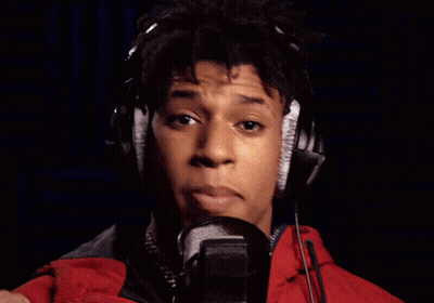 A Man Wearing Headphones Sings Into A Microphone In Front Of A Neon Open Sign GIF