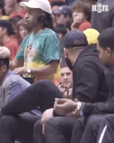A Man Wearing Headphones Sits In A Crowd Of People At A Basketball Game . GIF