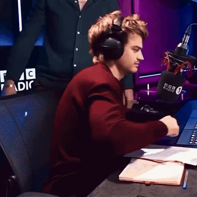 A Man Wearing Headphones Sits In Front Of A Microphone That Says Bbc Radio 0 GIF