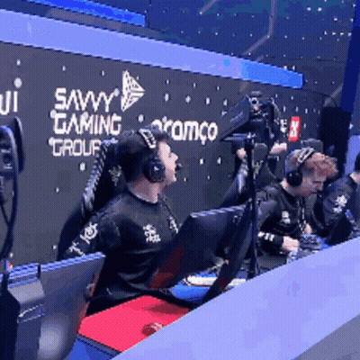 A Man Wearing Headphones Sits In Front Of A Savvy Gaming Group Sign GIF