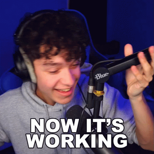 A Man Wearing Headphones Stands In Front Of A Blue Microphone And Says " Now It 'S Working " GIF