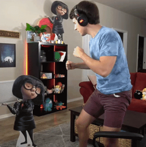A Man Wearing Headphones Stands In Front Of A Cardboard Cutout Of Edna GIF