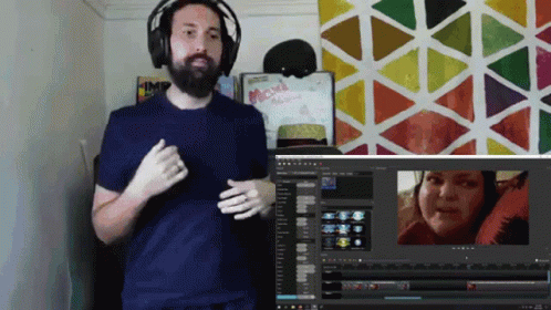 A Man Wearing Headphones Stands In Front Of A Computer Screen With A Sign That Says Maxi On It GIF