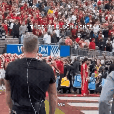 A Man Wearing Headphones Stands In Front Of A Crowd At A Football Game And Says The $ 1.50 Busch Lights Me . GIF