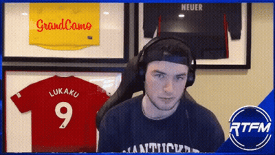A Man Wearing Headphones Stands In Front Of A Display Of Jerseys Including One That Says Lukaku 9 GIF
