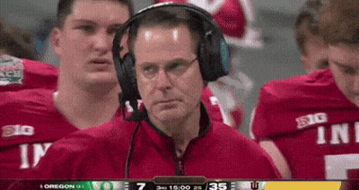 A Man Wearing Headphones Stands In Front Of A Group Of Football Players Wearing Red Jerseys That Say Big GIF
