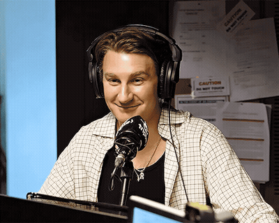 A Man Wearing Headphones Stands In Front Of A Microphone GIF