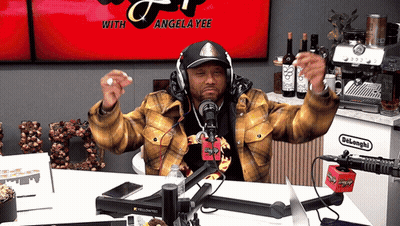 A Man Wearing Headphones Stands In Front Of A Microphone With Angela Yee On The Screen GIF